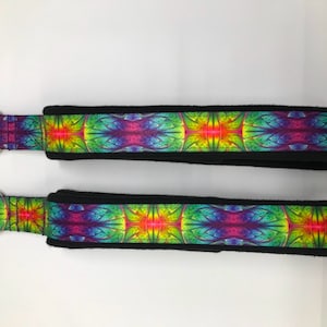 May include: Two black and rainbow colored fabric straps with metal rings on one end. The straps have a colorful, abstract design.