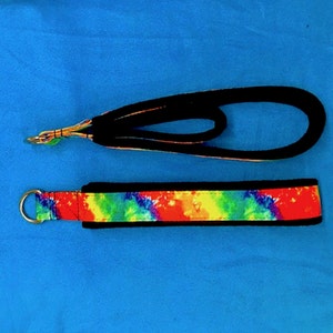May include: A tie-dye fabric leash with a black trim and a silver ring. The leash is on a blue background.