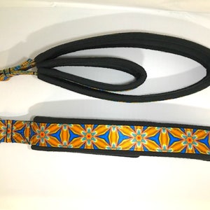 May include: A black and orange dog collar with a geometric pattern. The collar has a silver metal ring on one end and a black padded loop on the other end.