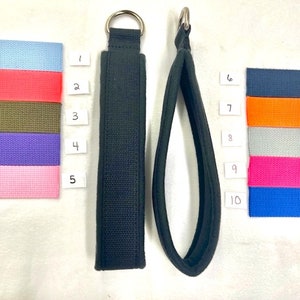 以下が含まれることがあります： 銀色の金属製のリングが付いた黒い布製のループが2つ。ループはサイズと形が異なります。小さいループは、両端にリングが付いたストレートストラップです。大きいループは、上部にリングが付いた円形です。ループは白い表面にあります。