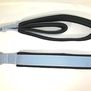 Puede incluir: Dos correas de ejercicio azul claro con bordes negros y anillos metálicos plateados. Las correas están hechas de tejido tejido y tienen una sección acolchada.