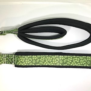 May include: A black and green fabric strap with two metal rings. The strap has a green floral pattern.