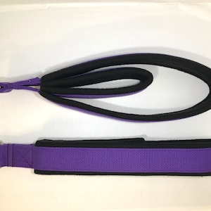 May include: Two purple straps with black edging and metal rings. The straps are made of a woven fabric and have a padded section.