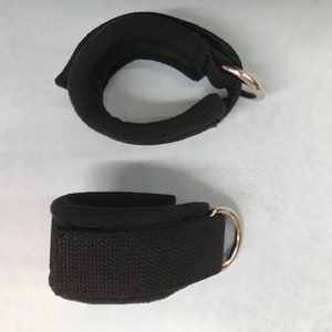 May include: Two black ankle straps with metal rings. The straps are made of a soft, padded material and have a secure closure.