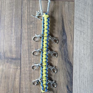 May include: A yellow and blue paracord keychain with multiple silver key rings. The keychain has a large silver carabiner at the top.