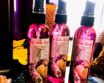 May include: Three pink spray bottles labeled "Sacred Space Spray" with a cedar blend. Each bottle features a label with text and an image of a sage bundle and crystals. The bottles have black spray nozzles.