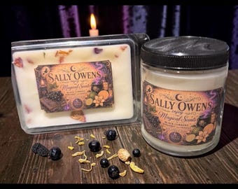 May include: A rectangular wax melt container and a cylindrical glass candle jar with a black lid. Both feature labels reading Sally Owens Magical Scents Black Currant Bergamot Vanilla. Dried flower petals and dark berries are scattered nearby.