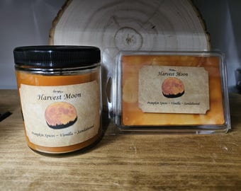 May include: A jar candle and a wax melt, both labeled "Harvest Moon." The candle is in a glass jar with a black lid. The wax melt is in a clear plastic container. Both have labels with a moon graphic and the scent notes: Pumpkin Spices, Vanilla, Sandalwood.