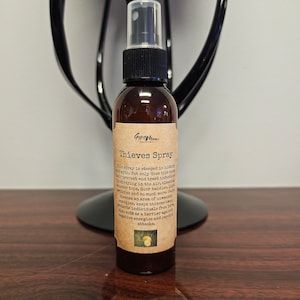 May include: A brown glass spray bottle with a black cap and a clear spray nozzle. The label reads "Thieves Spray" and includes text about its use. The bottle is on a wooden surface.