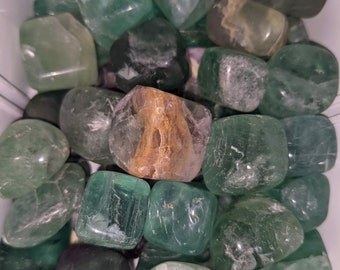 May include: A collection of tumbled green fluorite stones. The stones are various shades of green and some have white streaks. The stones are smooth and polished.