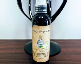 May include: A small, dark glass bottle with a white spray nozzle. The bottle is labeled "Midnight Margarita Spray" and has a small illustration of a margarita glass and a lime wedge. The label also includes the text "When life gives you limes, make margaritas."