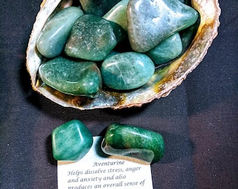 May include: A collection of polished green aventurine stones displayed in a natural shell. The stones vary in size and shape, with a glossy finish. A small card with text about aventurine is also present.