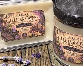 May include: A wax melt clamshell and a glass jar candle, both featuring labels with the text Gilllian Owens Witchy + Magical + Sassy with the Magical Scents of Black Cherry, Patchouli, and Sandalwood with a pinch of orange, alongside purple crystals and lavender.
