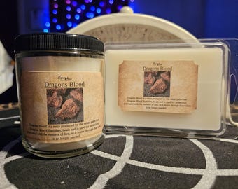May include: A glass jar candle and a wax melt, both labeled "Dragons Blood." The labels feature an image of reddish-brown resin. The candle has a black lid. The wax melt is in a clear plastic container.