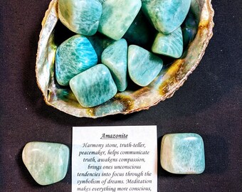 May include: A collection of smooth, green Amazonite stones in a seashell. The stones are tumbled and have a natural, earthy look. The text on the card reads: "Amazonite Harmony stone, truth-teller, peacemaker, helps communicate truth, awakens compassion, brings ones unconscious tendencies into focus through the symbolism of dreams. Meditation makes everything more conscious, helps us manifest our dreams and desires."