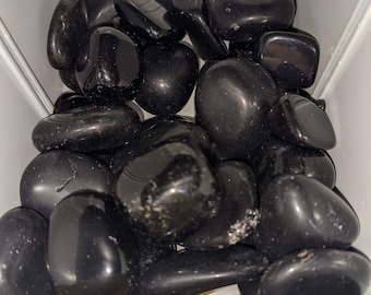 May include: A collection of smooth, black stones in a white container. The stones are various sizes and shapes, and they are piled high in the container.