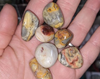 May include: A collection of seven tumbled stones with a variety of brown, yellow, and white patterns. The stones are smooth and polished.
