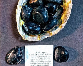May include: Black Onyx tumbled stones in a seashell. The stones are smooth and polished, with a deep black color. The text on the card reads "Black Onyx A protection stone. It is said that this stone holds the memories of the wearer. Offers protection during spiritual counseling, tarot card readings and other psychic influences."
