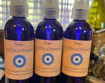 May include: Three blue glass spray bottles with clear spray nozzles. Each bottle has a label that reads "Evil Eye of Protection" with an eye symbol. The bottles are filled with a dark liquid.