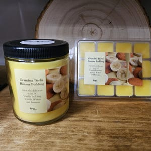 May include: Two yellow candles with a banana pudding scent. The candles are in glass jars with labels that say "Grandma Barbs Banana Pudding". The label also says "Enjoy the delicious scent of Vanilla Pudding, Vanilla Water and Banana".