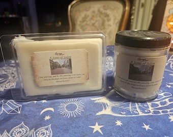 May include: Two scented wax melts and a candle with the text "A Scent of Salem". The wax melts are in a clear plastic container, and the candle is in a glass jar with a black lid. The labels feature a street scene.
