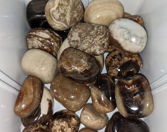 May include: A collection of tumbled stones in shades of brown, black, and white. The stones have a variety of patterns and textures.