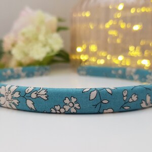 May include: A blue headband with a white floral pattern. The headband is made of fabric and has a simple design.