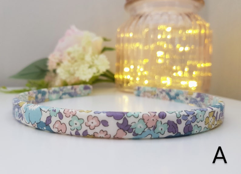 May include: A white headband with a floral pattern in shades of blue, purple, and pink. The headband is made of fabric and has a simple design.