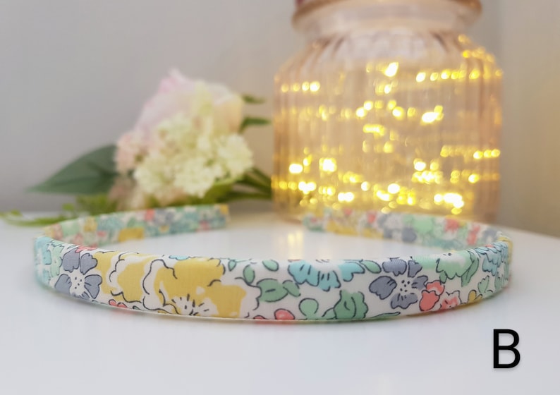 May include: A white headband with a floral print in shades of yellow, pink, blue, and green. The headband is made of fabric and has a simple design.