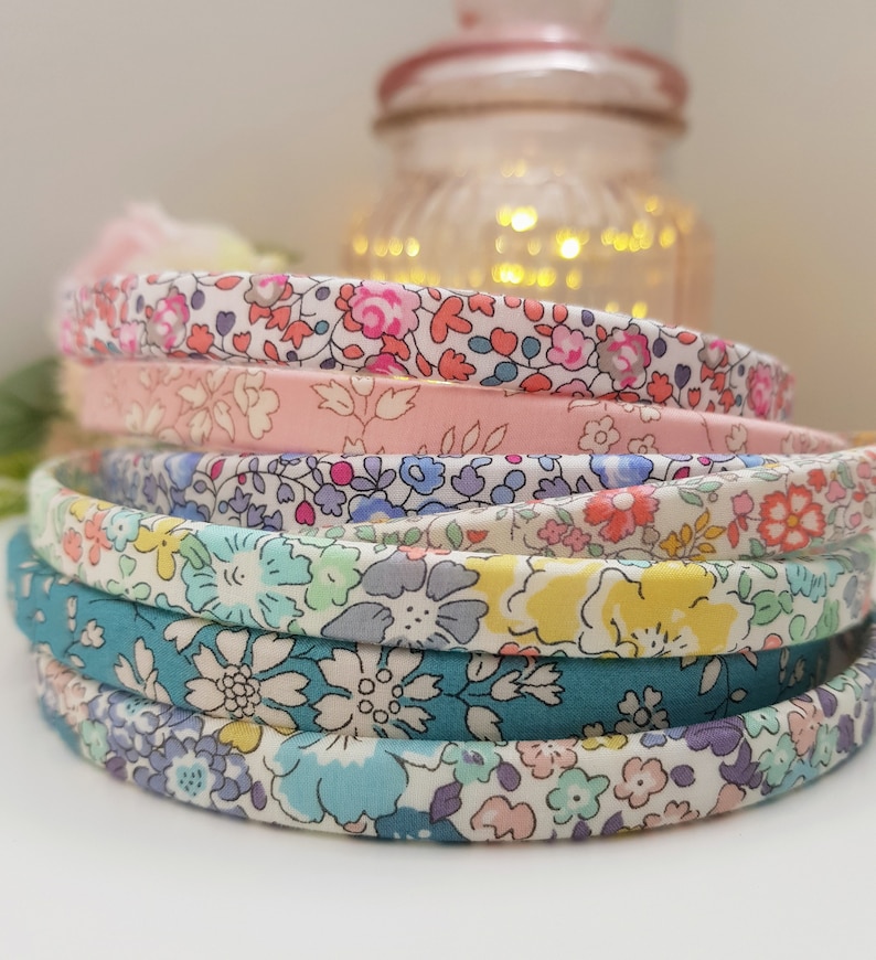 May include: A stack of five colorful fabric headbands with floral patterns. The headbands are made of a soft, stretchy fabric and are perfect for adding a touch of style to any outfit.