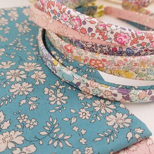 May include: A set of five floral patterned headbands in shades of pink, blue, and white. The headbands are made of fabric and have a simple design.