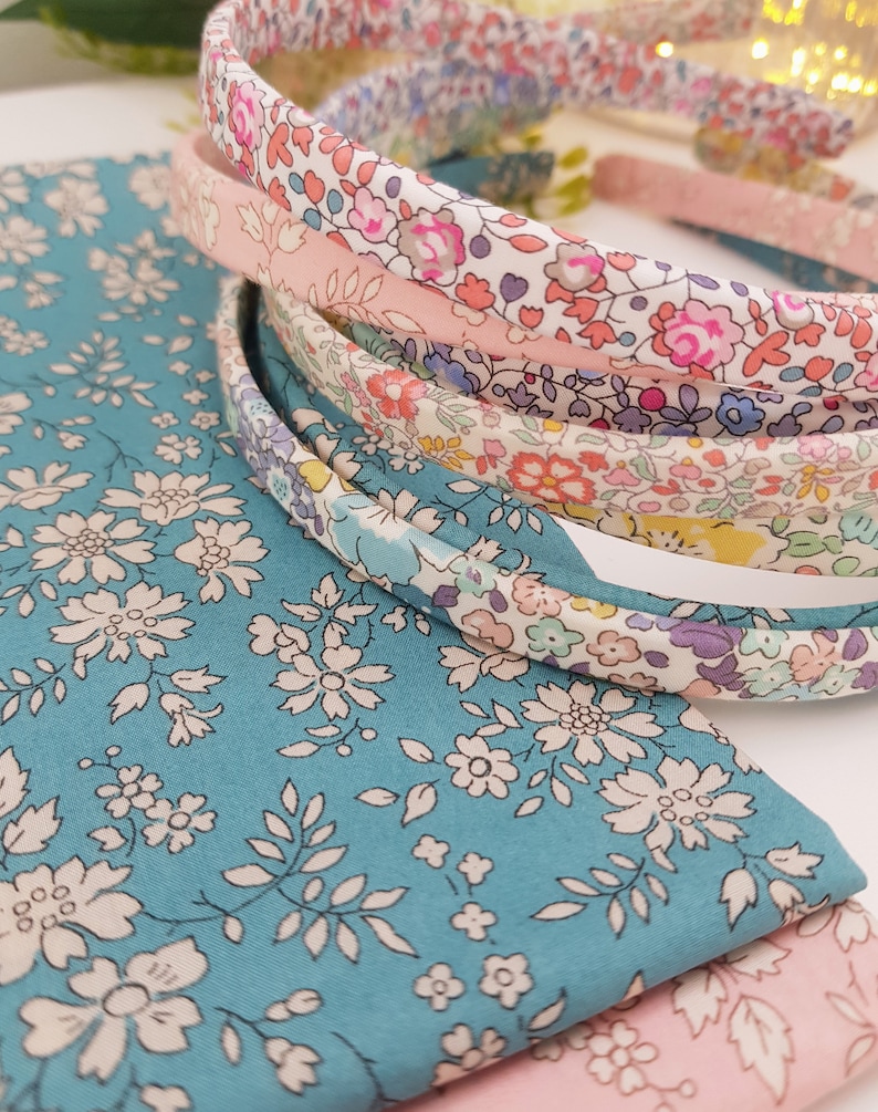 May include: A set of five floral patterned headbands in shades of pink, blue, and white. The headbands are made of fabric and have a simple design.