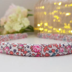 May include: A white headband with a floral print in pink, blue, and gray. The headband has a simple design and is made of fabric.