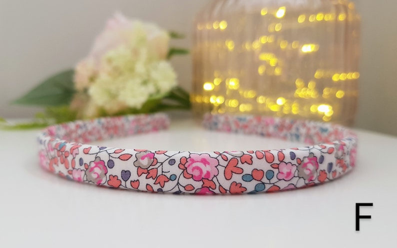May include: A white headband with a floral print in pink, blue, and gray. The headband has a simple design and is made of fabric.