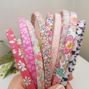 May include: A collection of colourful fabric-covered headbands with floral patterns. The headbands are pink, blue and white with various floral designs.