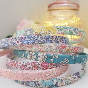 May include: A stack of colorful floral patterned headbands. The headbands are made of fabric and are in shades of pink, blue, green, and yellow.