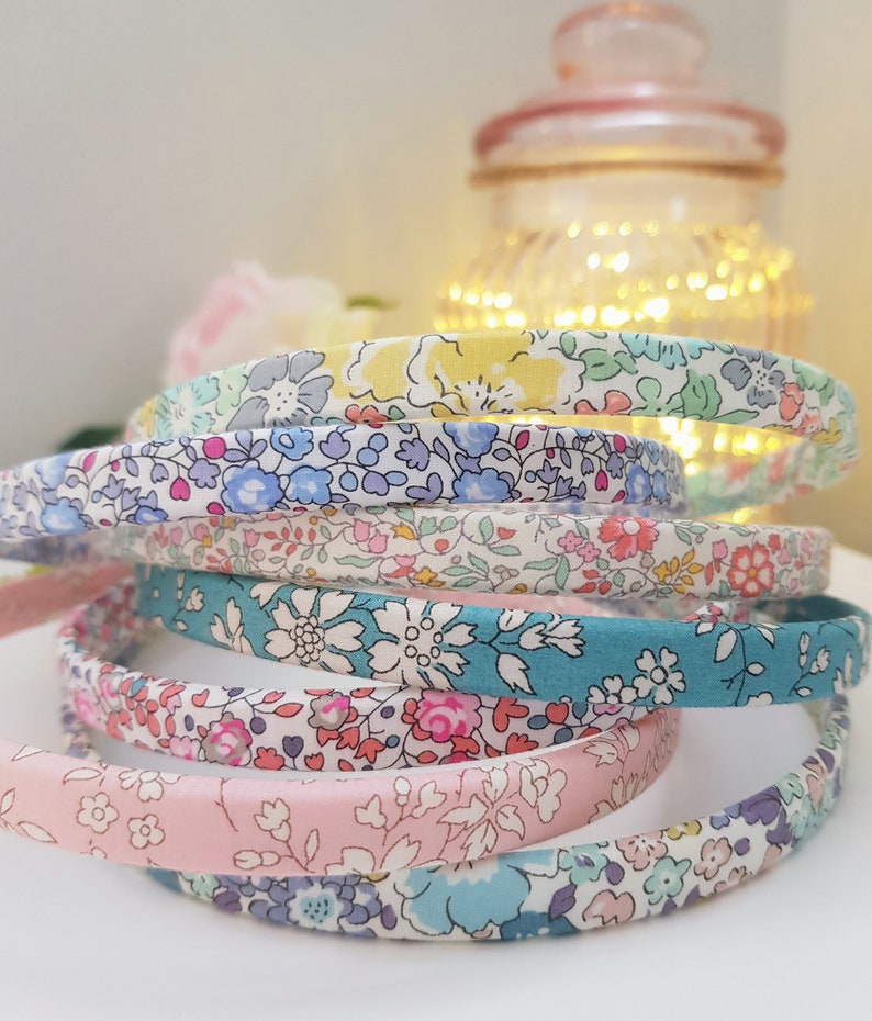 May include: A stack of colorful floral patterned headbands. The headbands are made of fabric and are in shades of pink, blue, green, and yellow.