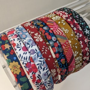 May include: A set of 10 colourful fabric headbands with floral and geometric patterns. The headbands are arranged in a stack, with the most colourful headband at the top.