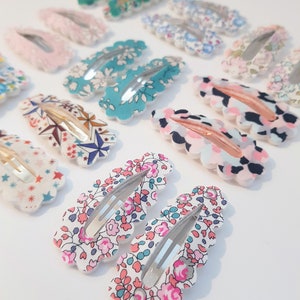 May include: A set of 12 colorful hair clips with various floral and geometric patterns. The clips are made of fabric and have a scalloped edge.