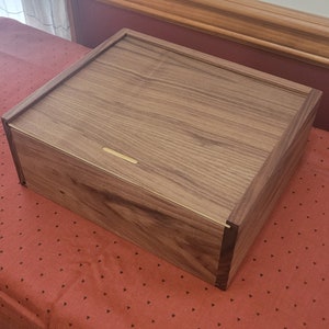 May include: A wooden box with a hinged lid and a brass latch. The box is made of walnut wood and has a natural finish.
