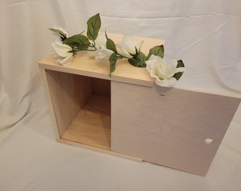 May include: A light wood box with a sliding door. The box is decorated with a garland of white flowers.