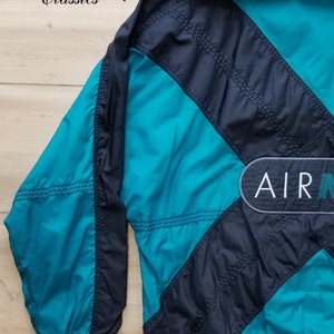 May include: A black and teal blue windbreaker jacket with a large "AIR" logo on the back. The jacket has a zipper closure and a stand-up collar.