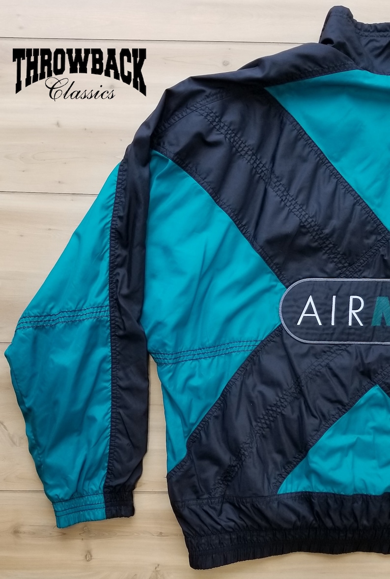 May include: A black and teal blue windbreaker jacket with a large "AIR" logo on the back. The jacket has a zipper closure and a stand-up collar.