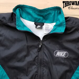 May include: Black and teal windbreaker jacket with a zipper closure and a Nike logo on the front. The jacket has a white tag with the Nike logo and size information.