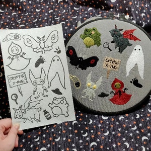 Może przedstawiać: Arkusz rysunku czarno-białego z różnymi ilustracjami kryptyd, w tym motylem, duchem, żabą, stworzeniem z dużymi uszami i stworzeniem z długim ogonem. Arkusz zawiera również tekst "Cryptid X-ing."