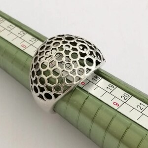 May include: A silver ring with a geometric, honeycomb-like design. The ring is sized on a ring sizer, showing a size 18.