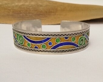 Puede incluir: Un brazalete de plata con un diseño de esmalte colorido. El diseño presenta remolinos y puntos azules, verdes y amarillos.