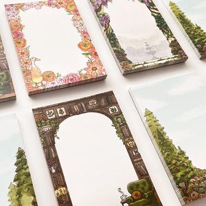 Può includere: Una collezione di blocchi per appunti illustrati con varie scene. Alcuni blocchi hanno bordi floreali, mentre altri raffigurano archi con temi di giardino e biblioteca. La tavolozza dei colori include verdi, marroni e tenui pastelli.