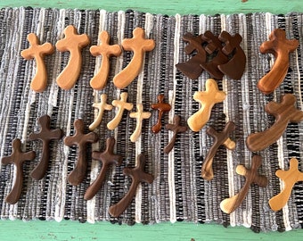 May include: A collection of wooden crosses in various sizes and shades of brown and natural wood. The crosses are arranged on a woven rug with a black and white pattern.