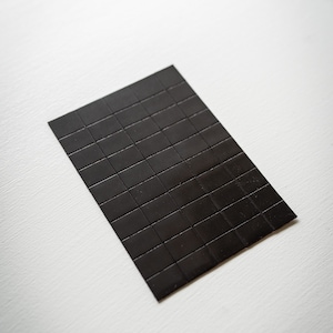 Op de afbeelding: Een zwarte magnetische plaat met een rasterpatroon. De plaat is gemaakt van kleine vierkanten.